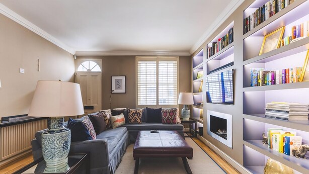 A living room with a sectional sofa, a coffee table, a bookshelf, and a fireplace. - Stylish Chelsea Escape With Charm (London)