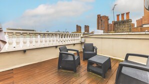 A rooftop terrace with wicker furniture, a balustrade, and a cityscape view. - Stylish Chelsea Escape With Charm (London)