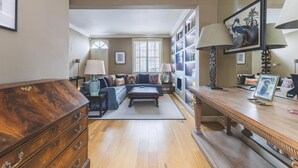 A living room with a sectional sofa, a wooden coffee table, a bookshelf, and a large window. - Stylish Chelsea Escape With Charm (London)