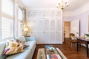 Ein Wohnzimmer mit einer Couch, einem Couchtisch, einer Chandelüster und weißen, verschlossenen Schränken.