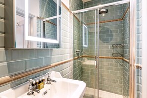 A bathroom with a glass-enclosed shower, a white sink with multiple faucets, and a mirror above the sink. - Elegant English Retreat Near Maida Vale (London)