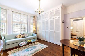 A living room with a sofa, coffee table, and a large window with blinds. - Elegant English Retreat Near Maida Vale (London)