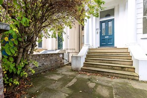 A building with a blue door, a set of stone steps leading to the entrance, and a tree with green leaves beside the building. - Elegant English Retreat Near Maida Vale (London)