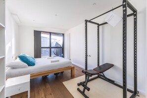 Quarto com cama, um banco, barra de exercícios e janela.