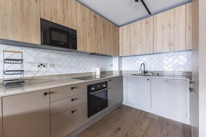A modern kitchen with wooden cabinets, a Bosch microwave, a built-in oven, and a herringbone-patterned backsplash. - Large Bright Canal 1-bed With Balcony (London)