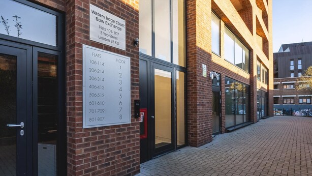 A brick building with a sign indicating the location of Waters Edge Court Exchange, including a floor number sign. - Large Bright Canal 1-bed With Balcony (London)