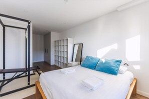A modern bedroom with a bed, a workout station, a large mirror, and a storage unit. - Large Bright Canal 1-bed With Balcony (London)