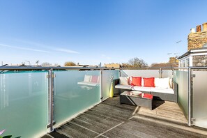 Eine Dachterrasse mit Glastrennwand, einer Sitzecke mit Kissen und Blick auf die Stadt.