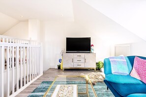 Ein Wohnzimmer mit Fernseher, einem blauen Sofa und einem weißen Babybett.
