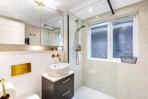 Ein modernes Badezimmer mit einem weißen Waschbecken, dunklen Schränken, einem großen Spiegel und einer Dusche mit einer Milchglasscheibe.