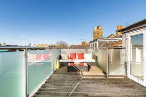 Eine Dachterrasse mit Sitzgelegenheit, einer Glasabtrennung und Blick auf die Stadtlandschaft.