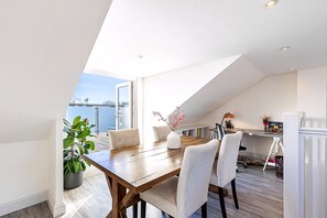Ein Essbereich mit einem Holztisch, Stühlen, einer Topfpflanze und Blick auf die Stadt.