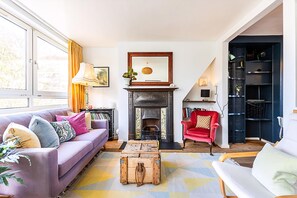 A living room with a fireplace, a sofa, a red armchair, a wooden chest, and a bookshelf. - Bright Bold Hackney Escape (London)