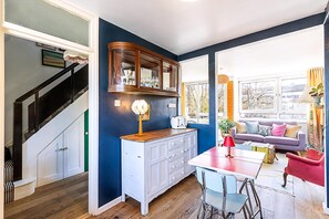 A modern kitchen with a wooden cabinet, a dining table with chairs, and a staircase leading to another level. - Bright Bold Hackney Escape (London)