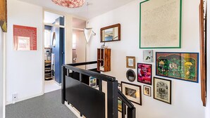 A staircase with a black handrail, a hanging pink chandelier, and various framed artworks on the walls. - Bright Bold Hackney Escape (London)