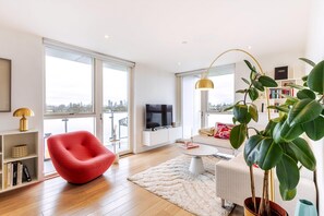 A modern living room with a red chair, a white sofa, a large plant, and a TV. - wba Contemporary Parkside Retreat (London)