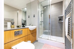 A modern bathroom with a glass-enclosed shower, a wooden vanity, a white sink, and a large mirror. - wba Contemporary Parkside Retreat (London)