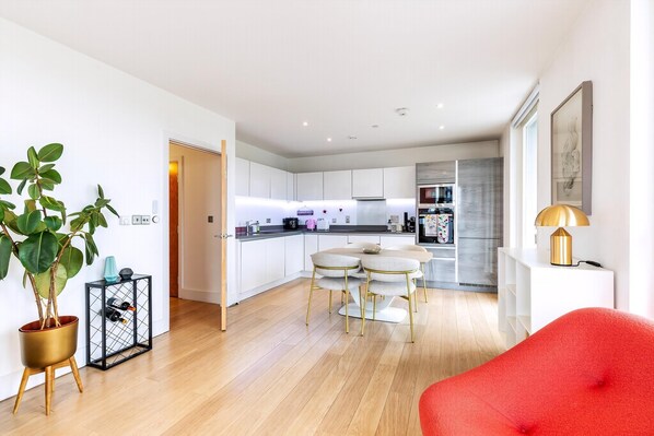 A modern kitchen with white cabinets, a dining area with a round table and chairs, and a red chair in the foreground. - wba Contemporary Parkside Retreat (London)