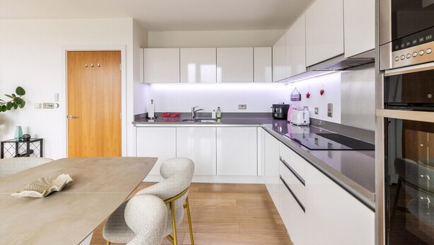 A modern kitchen with white cabinets, a stainless steel stove, and a wooden door. - wba Contemporary Parkside Retreat (London)