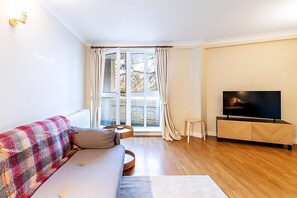 Ein Wohnzimmer mit Sofa, Fernseher, Holzschrank und einem Fenster mit Vorhängen.