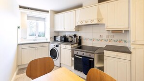 A compact kitchen with a washing machine, oven, microwave, and a window with a view. - Bright Canada Water Waterside Retreat (London)