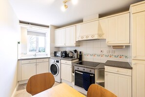 A compact kitchen with a washing machine, oven, microwave, and a window with a view. - Bright Canada Water Waterside Retreat (London)