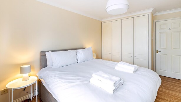 A hotel room with a bed, bedside lamp, wardrobe, and a door. - Bright Canada Water Waterside Retreat (London)