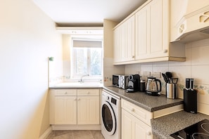 A compact kitchen with a washing machine, a coffee maker, and a microwave. - Bright Canada Water Waterside Retreat (London)