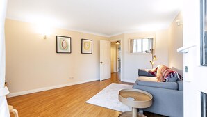 A modern living room with hardwood flooring, a grey sofa, a round wooden coffee table, and two framed artworks on the wall. - Bright Canada Water Waterside Retreat (London)