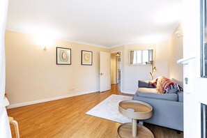 A modern living room with hardwood flooring, a grey sofa, a round wooden coffee table, and two framed artworks on the wall. - Bright Canada Water Waterside Retreat (London)