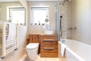 A modern bathroom with a toilet, vanity, bathtub, and a shower area. - Bright Stylish Kentish Town Retreat (London)