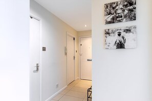 A hallway with white walls, a tiled floor, and two doors. There are two framed pictures on the wall. - Bright Stylish Kentish Town Retreat (London)