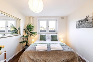 A bedroom with a bed, two bedside lamps, a large window, a mirror, a zebra painting, and a potted plant. - Bright Stylish Kentish Town Retreat (London)