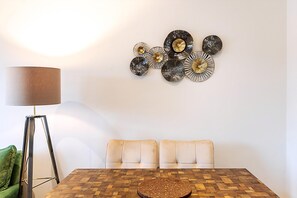 A dining area with a wooden table, two cushioned chairs, a floor lamp, and a wall-mounted decorative piece. - Bright Stylish Kentish Town Retreat (London)