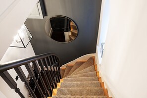Eine Treppe mit einem gewebten Teppich, einem runden Spiegel und einem schwarzen Geländer.