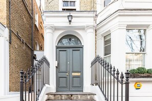 A double door with a small window above it, flanked by black iron railings and a white wall. - Stylish Notting Hill Apartment With Roof Terrace (London)