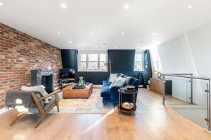 A modern living room with a brick wall, a fireplace, a blue sofa, and a wooden floor. - Stylish Notting Hill Apartment With Roof Terrace (London)