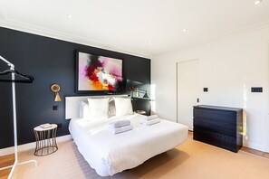 Ein modernes Hotelzimmer mit einem großen Bett, einem Flachbildfernseher, einem Schreibtisch und einem an der Wand hängenden Kunstwerk.
