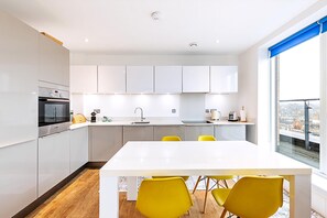 Eine moderne Küche mit weißen Schränken, einem eingebauten Ofen und einem Essbereich mit weißem Tisch und gelben Stühlen.