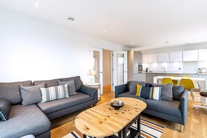 Ein modernes Wohnzimmer mit zwei Sofas, einem Couchtisch und einer Küche im Hintergrund.