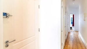Un pasillo con suelo de madera, paredes blancas y una puerta con picaporte y cerradura plateados.