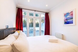 A hotel room with a bed, a window with curtains, a radiator, and a framed picture on the wall. - Colourful Three Bed Flat With Private Patio (London)