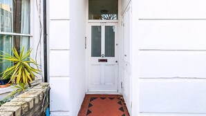 Una puerta blanca con un panel de vidrio, una pequeña planta en maceta y un suelo de baldosas con un diseño rojo y negro.