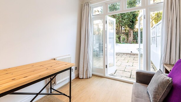 Una habitación con una mesa de madera, un sofá gris y un ventanal corredero que da a un patio exterior.