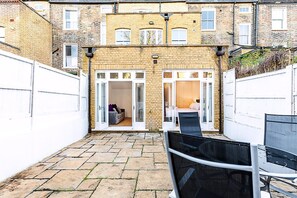 A courtyard with a brick building, a white door, and a chair. - Colourful Three Bed Flat With Private Patio (London)
