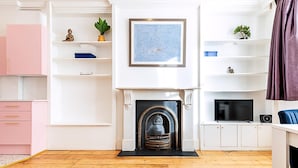Una sala de estar con chimenea, piso de madera, un sofá azul, un mueble rosa y un televisor.