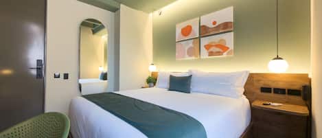 A hotel room with a bed, bedside tables, a mirror, and artwork on the wall.