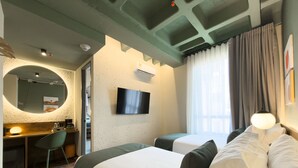 A hotel room with a bed, a desk with a chair, a television, and a window with curtains.