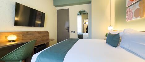 A hotel room with a bed, a desk, a chair, a TV, and a mirror.