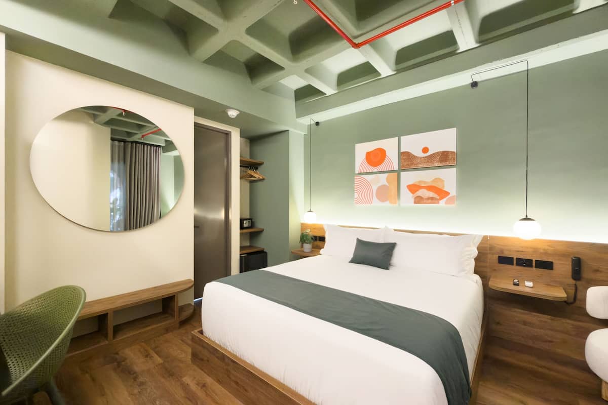 Una habitación de hotel moderna con una cama grande, un espejo redondo, un escritorio y un armario.